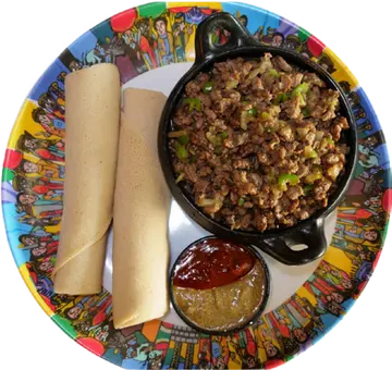 Dekak Tibs in a black dish beside a roll of injera.
