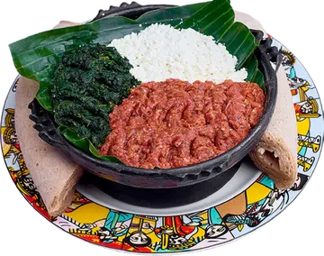 Kitfo with white cheese and greens on a plate with injera.