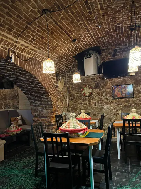 The main dining room under a brick vault: tables set with woven mesob baskets, and woven pendant lamps.